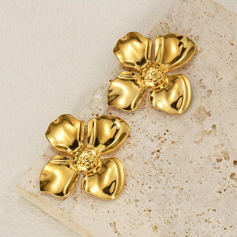 A pair of gold-plated stainless steel flower stud earrings with textured petals, displayed on a neutral stone background – perfect for wholesale jewelry suppliers like YanluoJewelry.