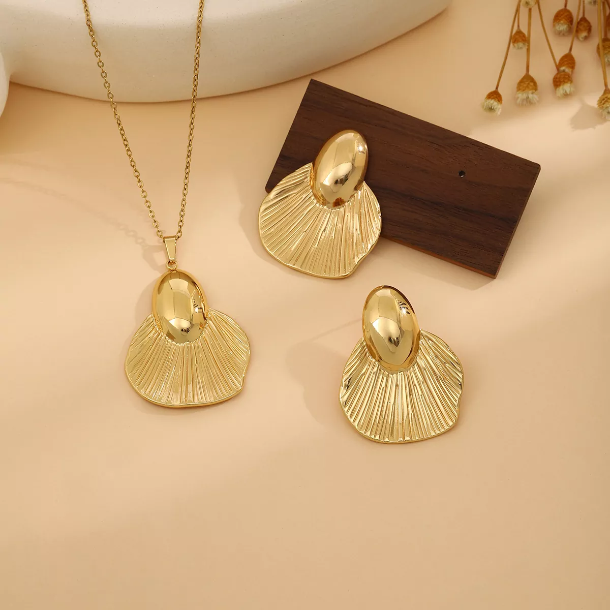 Fan-shaped gold stainless steel pendant and earrings set on beige background – offered by Yanluo Jewelry, a trusted stainless steel jewelry wholesale supplier
