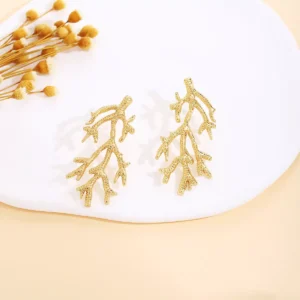 Gold coral branch design stainless steel earrings displayed on a white plate with dried flowers, elegant and nature-inspired wholesale jewelry.
