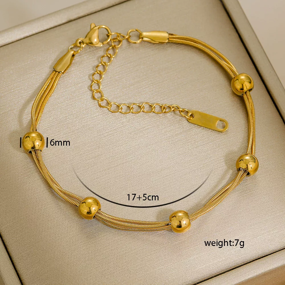 A triple-layered gold-tone stainless steel bracelet featuring a herringbone chain, a curb chain, and a box chain with adjustable extension (17+5cm), displayed on a beige jewelry box – ideal for bulk purchase from a stainless steel jewelry wholesale supplier.
