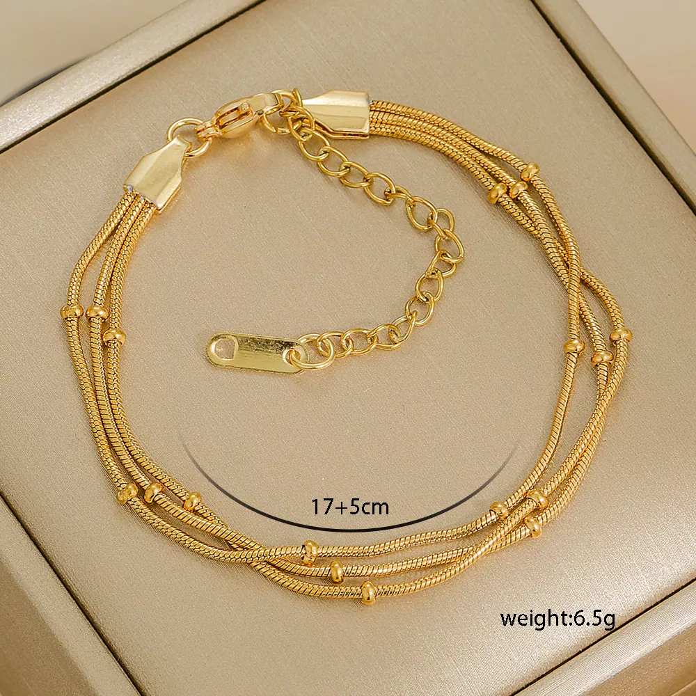 Gold multi-strand stainless steel bracelet with beaded accents, adjustable chain clasp, displayed on beige jewelry box