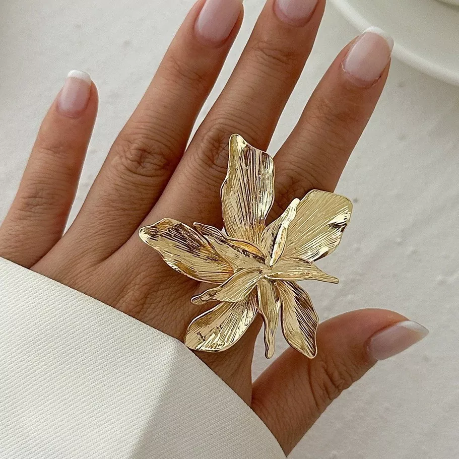 Close-up of a gold-plated stainless steel flower ring on a woman's hand, featuring detailed textured petals and statement design for wholesale jewelry supply.